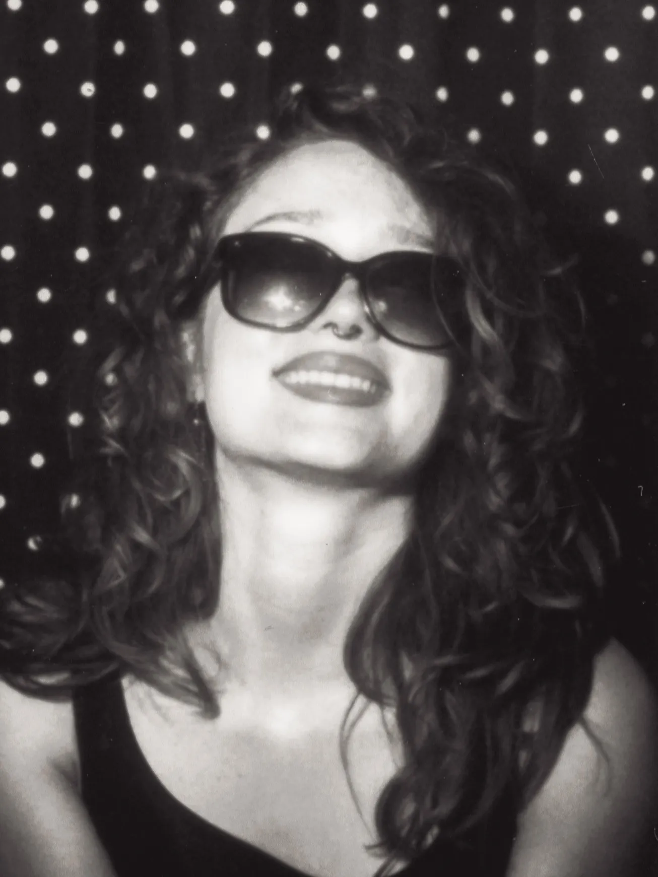 Enclosed photo booth black and white strip, frame one: sunglasses, head back, big smile