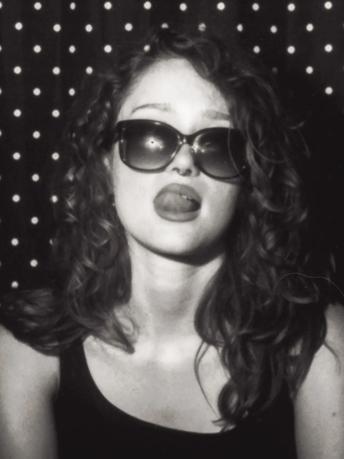 Enclosed photo booth black and white strip, frame two: tongue out behind the sunglasses