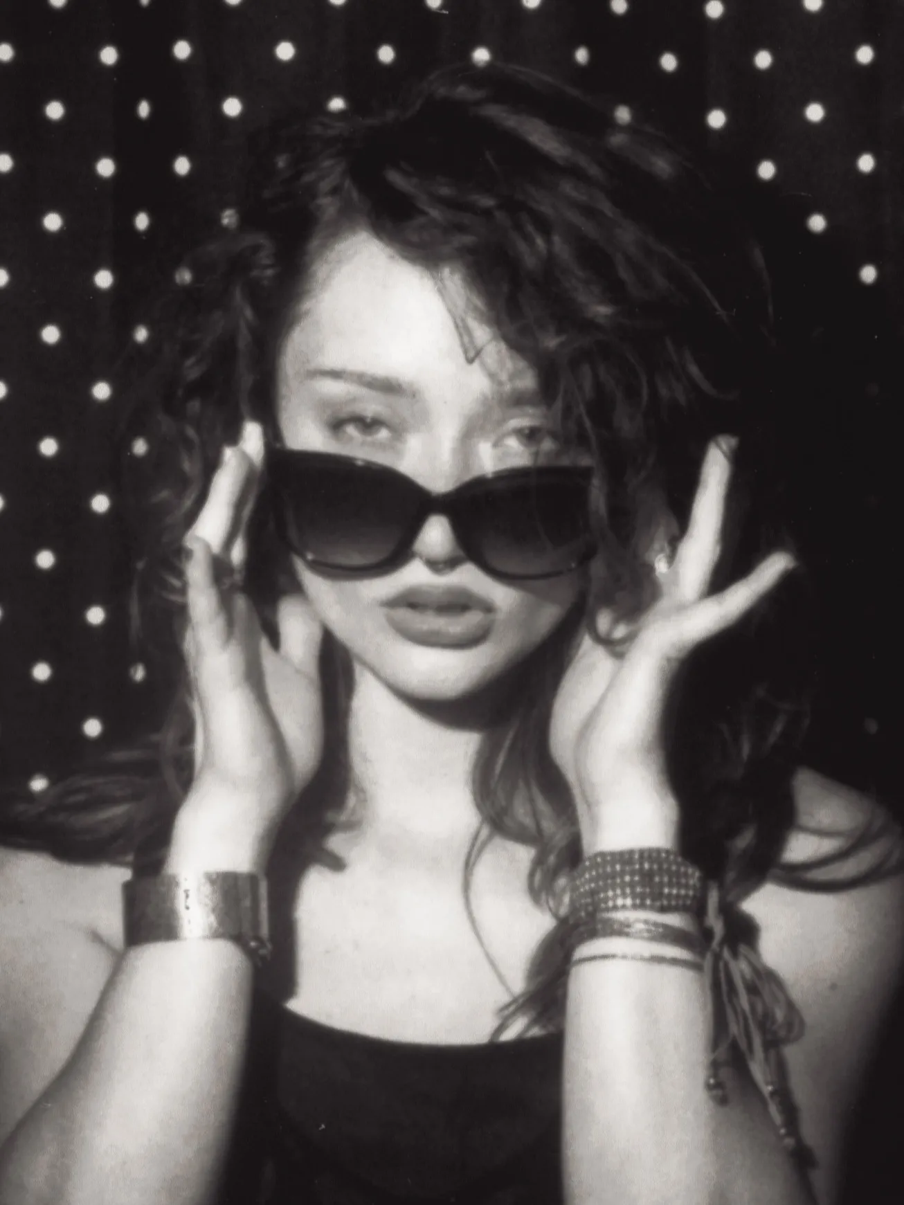 Enclosed photo booth black and white strip, frame four: sunglasses pulled down, eyes over the rims
