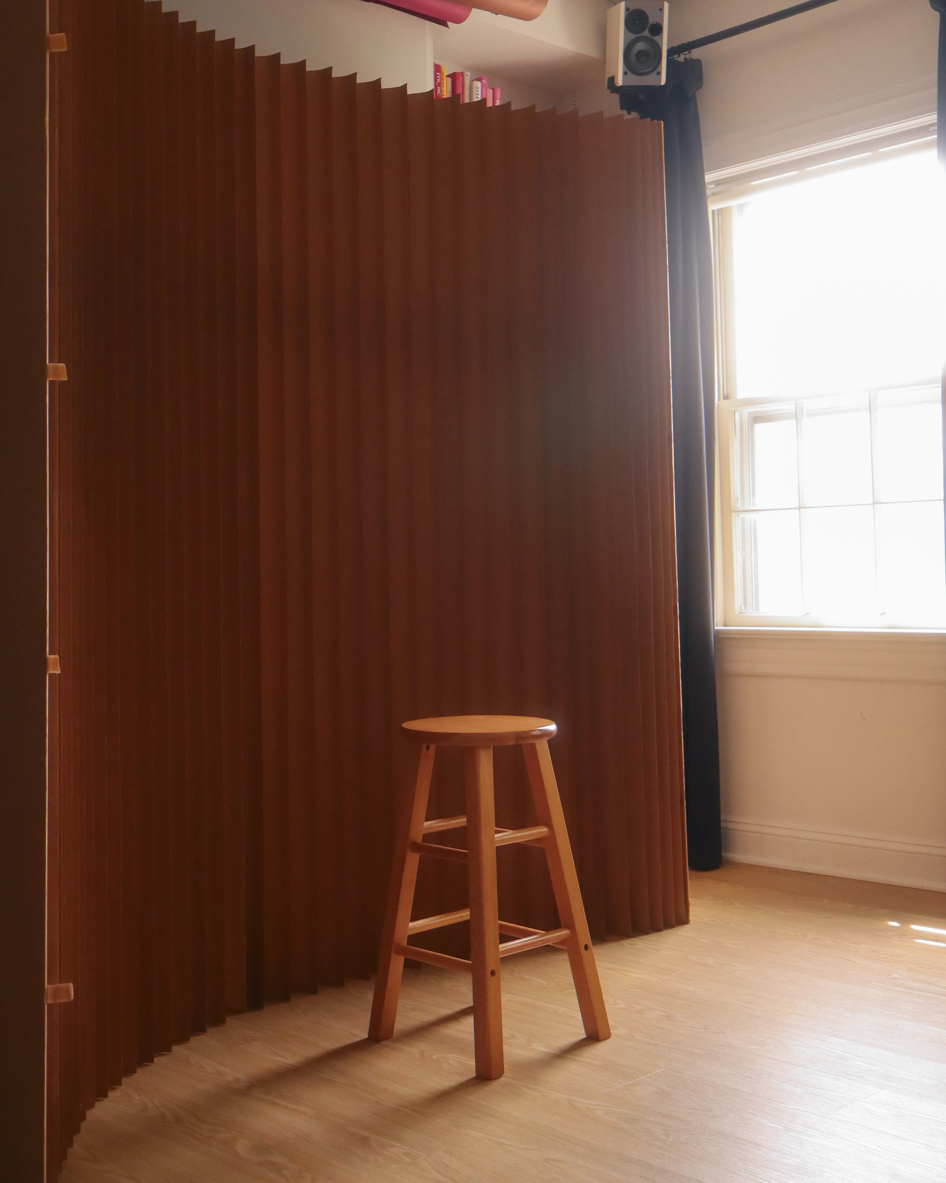 The Instant Booth, an open-air instant film photo booth setup in DC: a curved pleated paper backdrop, a wooden stool, and window light
