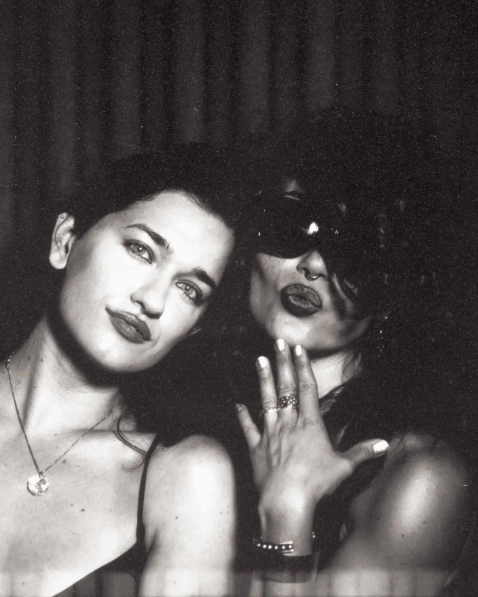 Black and white photo booth print: two friends cheek to cheek, one pouting in sunglasses with a hand raised