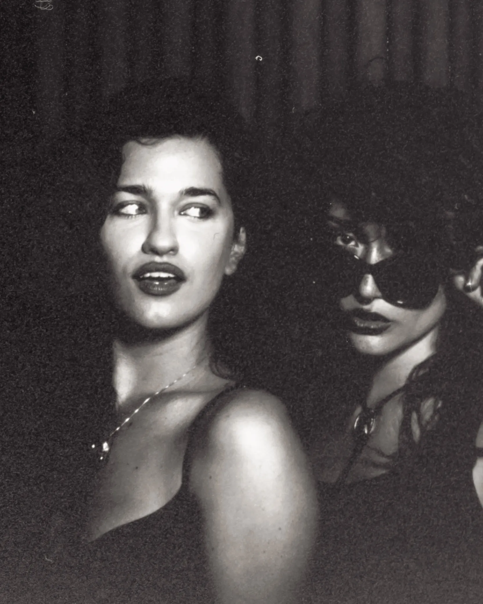 Black and white photo booth print: two friends in the booth, one glancing sideways, the other in sunglasses
